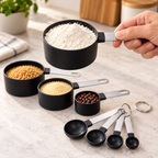 Vista del producto: set negro de cuatro tazas medidoras de plástico cilíndricas con mangos planos plateados de acero y cuatro cucharas medidoras negras redondas con mangos planos plateados, dos anillos metálicos de unión. Ambientación no incluida.