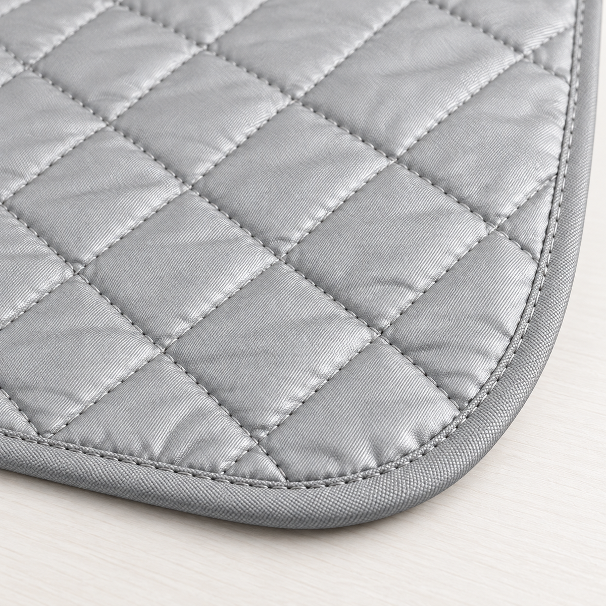 Tapete rectangular gris metálico para planchar de 48 x 84 cm, acolchado con costuras diagonales romboidales y ribete gris de esquinas redondeadas. — detalle del producto