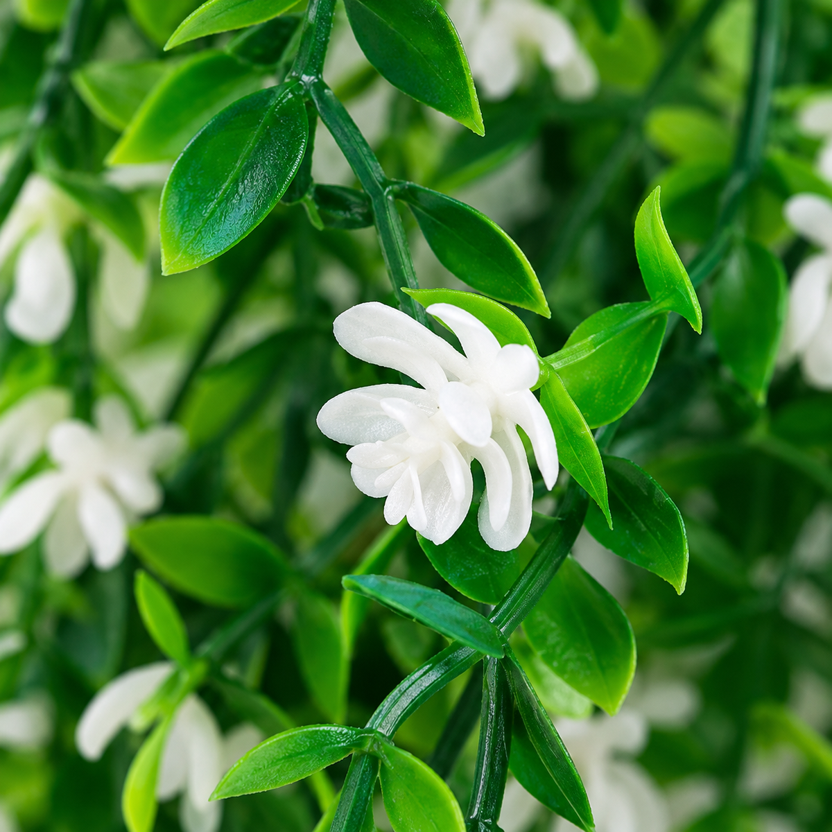 Planta artificial colgante de cinco tallos verdes con pequeñas hojas verdes y flores blancas alargadas de pétalos estrechos. — detalle del producto