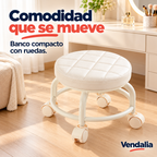 Banco bajo giratorio blanco con asiento redondo acolchado y costuras de cuadros, cuatro patas curvas unidas por aro circular y cuatro ruedas dobles crema — portada Vendalia