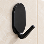 Gancho adhesivo negro con placa oval vertical y brazo corto inclinado — detalle del producto