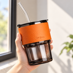 Detalle del vaso de vidrio con funda naranja, tapa negra y popote